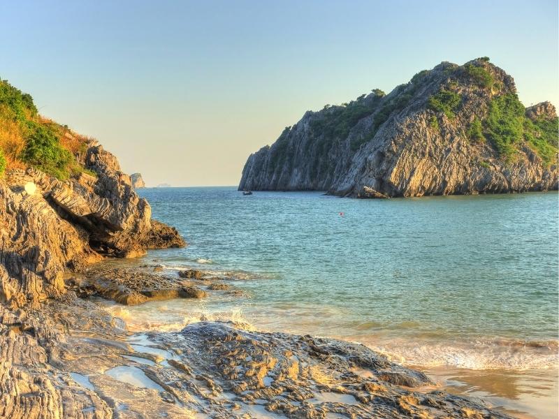 The rocky edge of a sandy beach on Cat Ba Island, looking out at another island