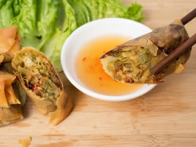 Chopsticks holding up a cha gio (Vietnamese deep fried spring roll) above a little white bowl of dipping sauce