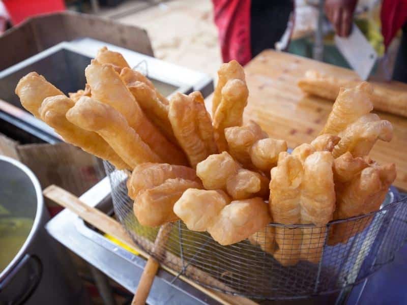 Sticks of chao quay, or deep fried dough, sticking up from a basket above a frier in Vietnam