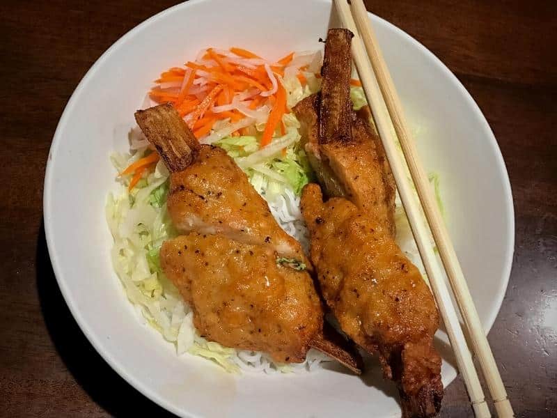 Vietnamese sugarcane shrimp on top of a bowl of rice noodles and veggies, with chopsticks across the bowl