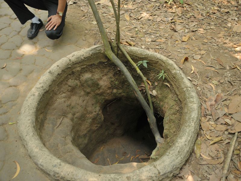 Looking down into a round tunnel down into the ground with a man kneeling down beside it