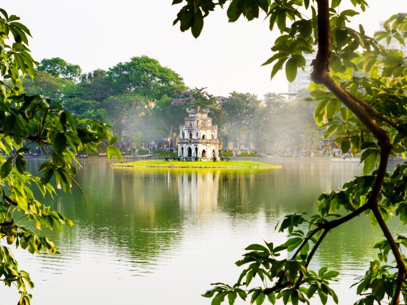 A misty lake with old white pagoda on a small island and tree branches framing the scene