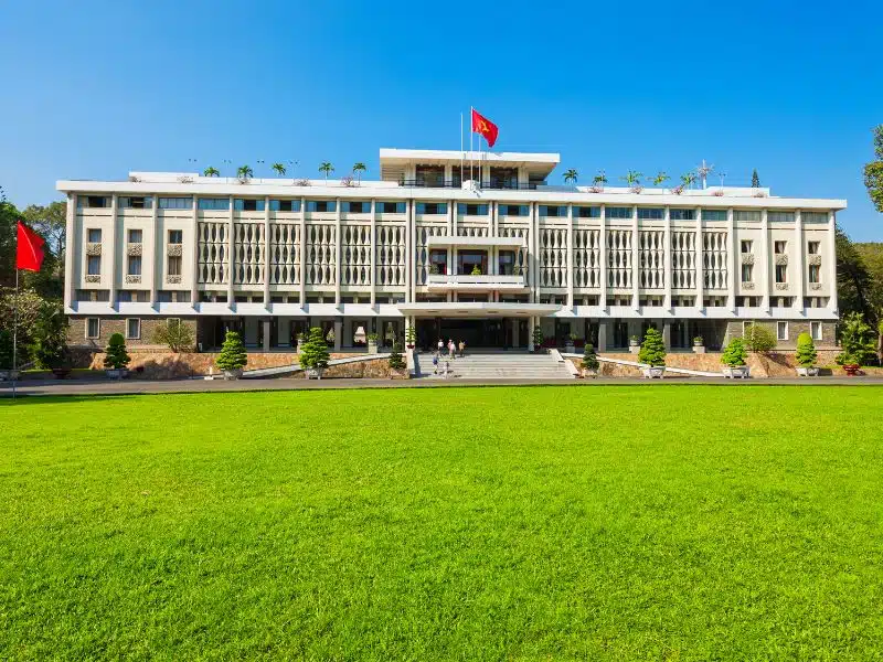 Exterior of the wide, white Independence Palace in Ho Chi Minh with grassy field in front