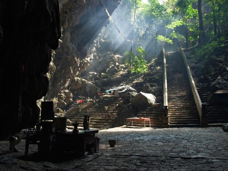 A dark shrine inside a cave at Perfume Pagoda in Vietnam, with stairs leading down into the cave and rays of sunlight