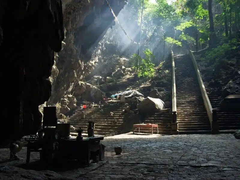 A dark shrine inside a cave at Perfume Pagoda in Vietnam, with stairs leading down into the cave and rays of sunlight