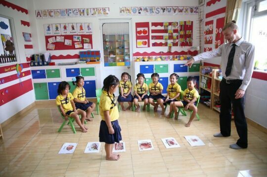 A foreign English teacher teaching a class of kids with uniforms on