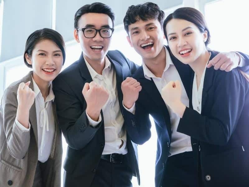 Two male and two female business people in Vietnam dressed in business clothing, smiling and pumping their fists