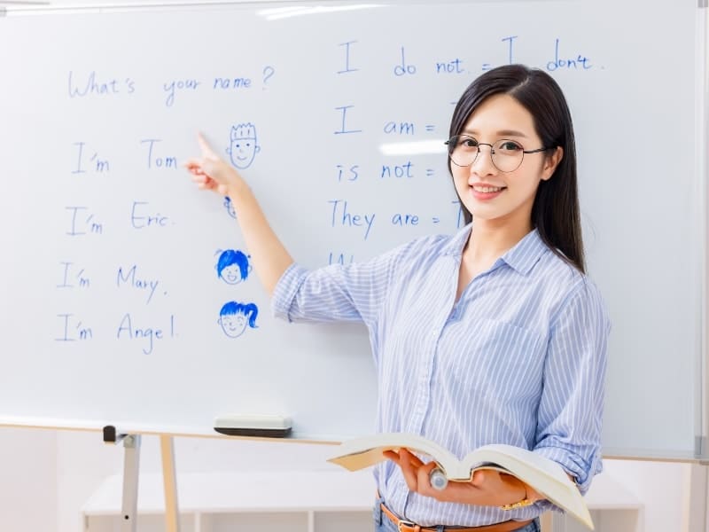 A female English teaching pointing at some words on the white board and wearing typical clothes suitable for teaching in Vietnam