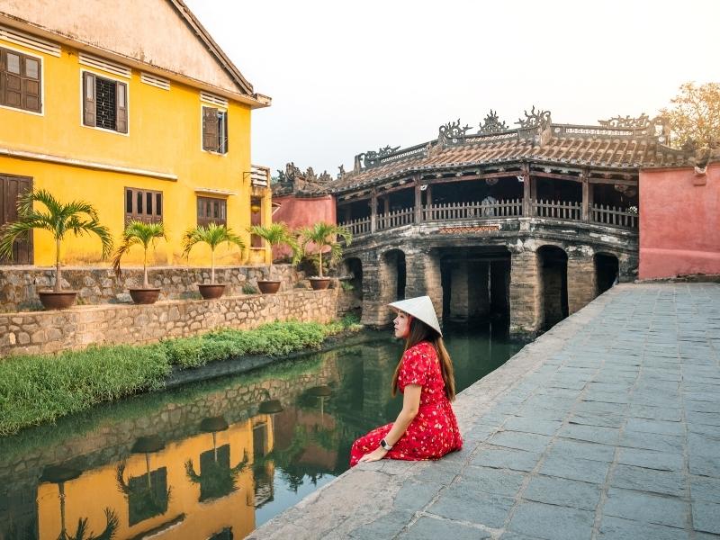 A female tourist in Vietnam wearing a red dress and conincal rice hat for taking a photo in front of the Japanese covered bridge in Vietnam