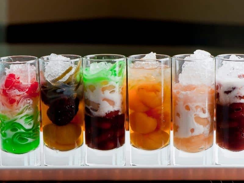 A row of glasses containing various jellies, fruits, and coconut milk