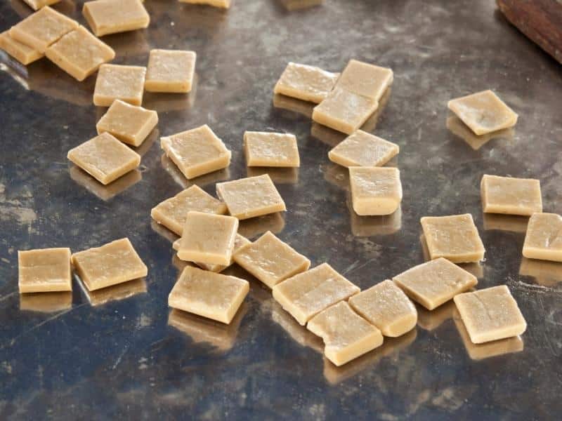 Some brown square-shaped coconut candies on a metal surface