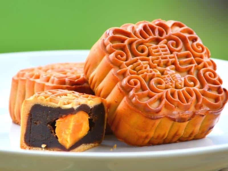 A plate of Vietnamese moon cakes, with one sliced into a quarter to see the bean and egg yolk inside